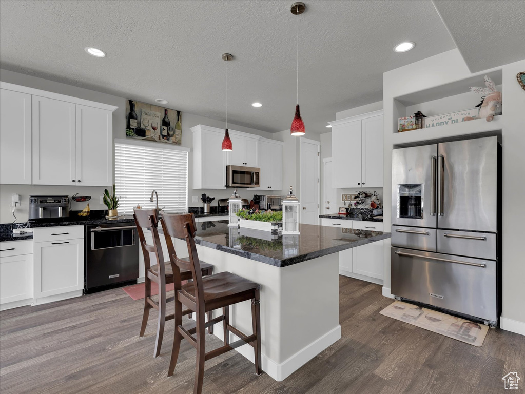 Kitchen featuring appliances with stainless steel finishes, a center island, hardwood / wood-style flooring, and white cabinetry
