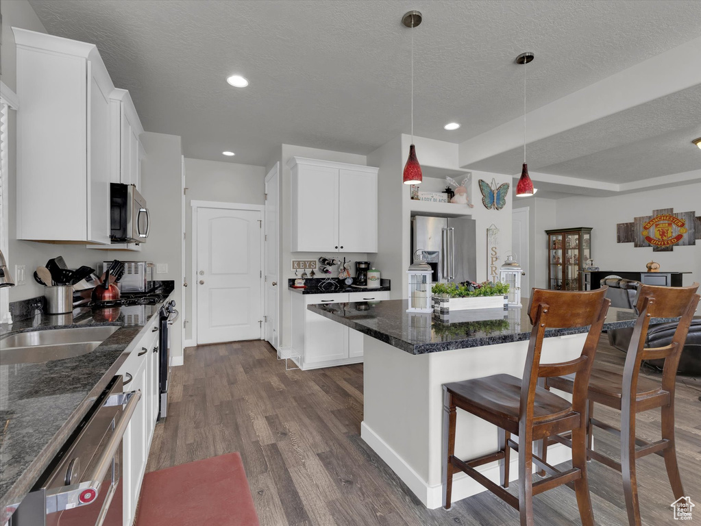 Kitchen featuring decorative light fixtures, appliances with stainless steel finishes, dark hardwood / wood-style floors, white cabinetry, and a center island