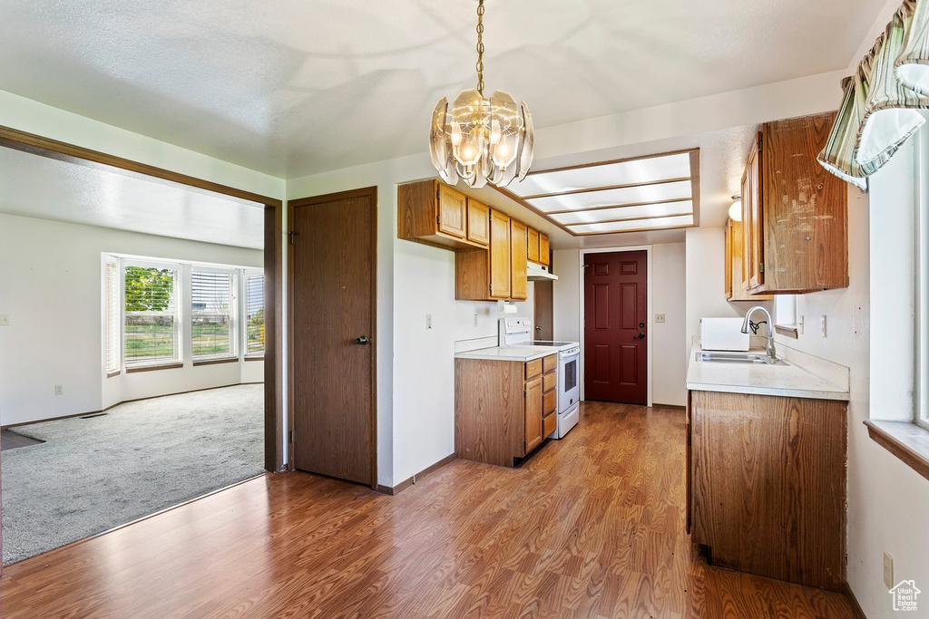 Kitchen featuring decorative light fixtures, carpet floors, electric stove, sink, and a chandelier