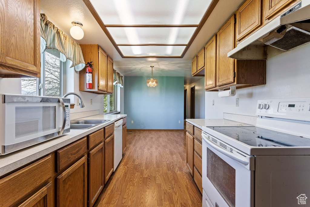 Kitchen with decorative light fixtures, sink, white appliances, and light wood-type flooring