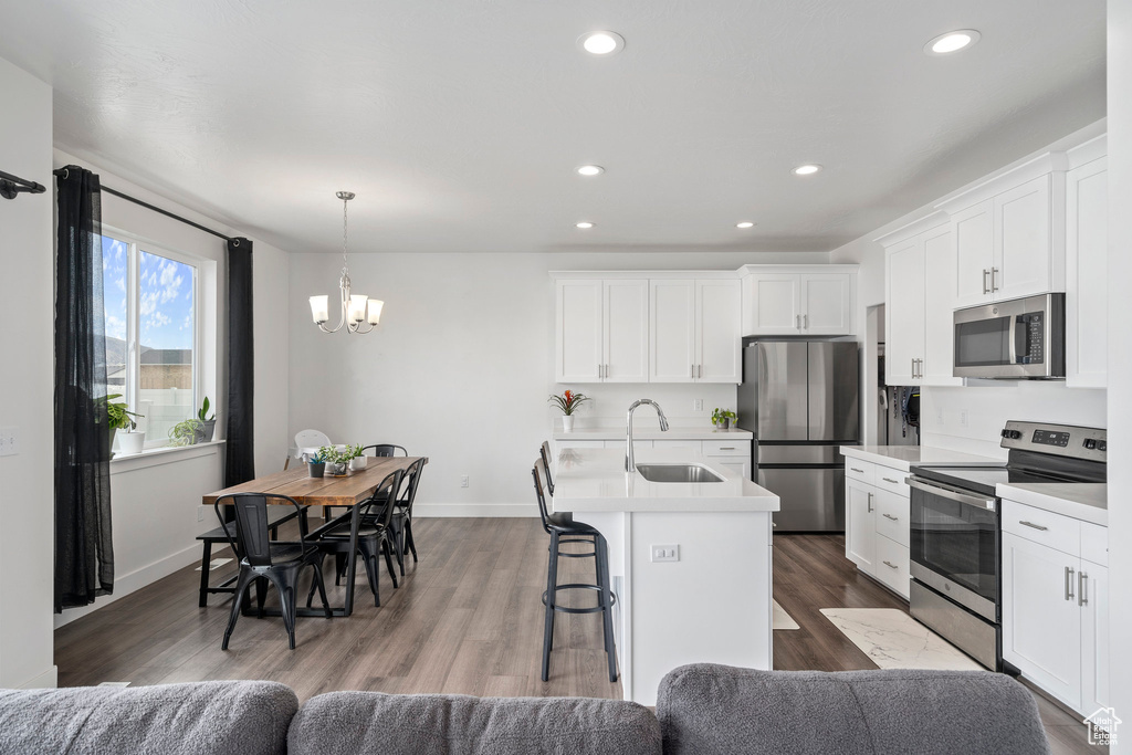 Kitchen featuring wood-type flooring, decorative light fixtures, stainless steel appliances, a center island with sink, and sink