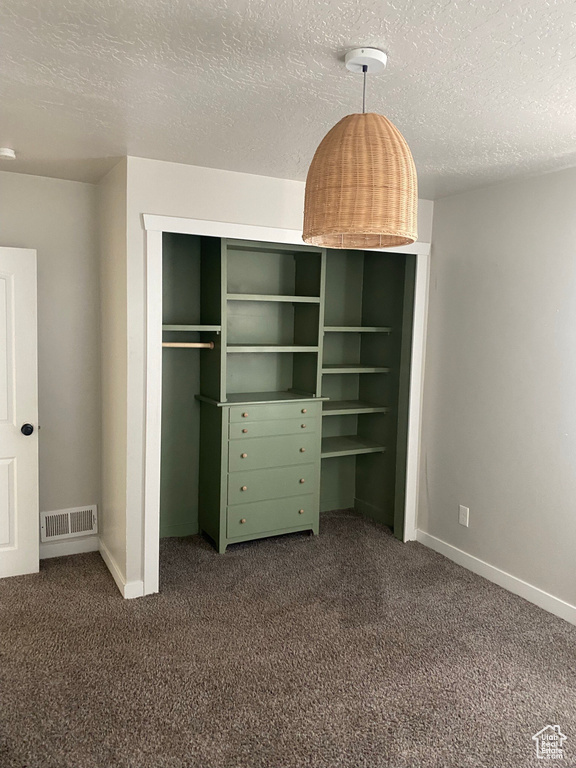 Unfurnished bedroom featuring a closet, a textured ceiling, and dark carpet
