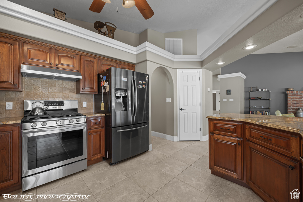Kitchen with backsplash, ceiling fan, stainless steel appliances, light stone counters, and light tile floors