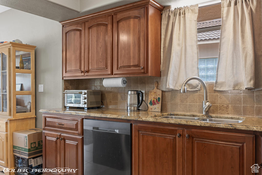 Kitchen featuring sink, tasteful backsplash, stone counters, and stainless steel dishwasher