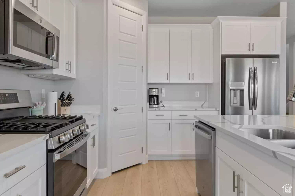 Kitchen with appliances with stainless steel finishes, light hardwood / wood-style floors, white cabinetry, and light stone counters