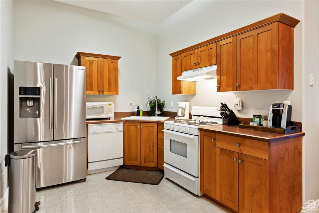 Kitchen featuring sink, white appliances, and light tile floors