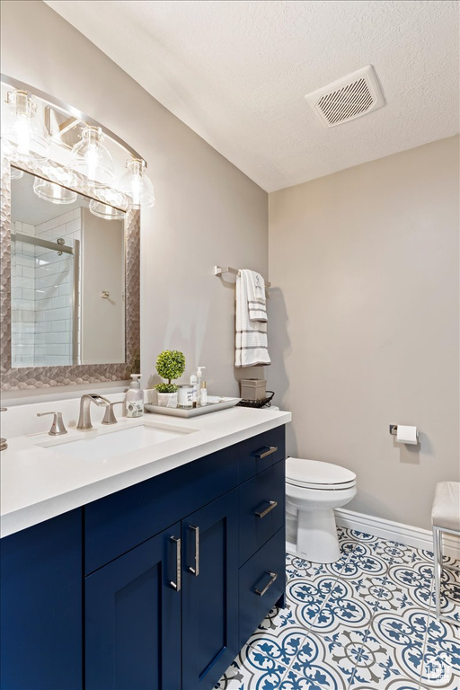 Bathroom with a textured ceiling, vanity, tile floors, and toilet