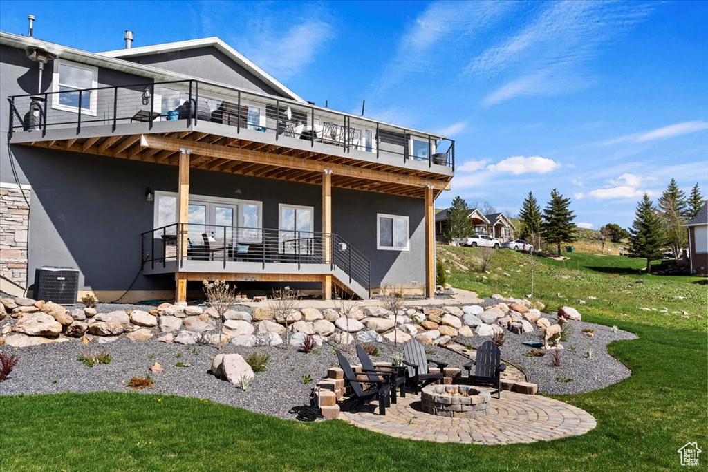 Back of house with an outdoor fire pit, a deck, a balcony, and a lawn