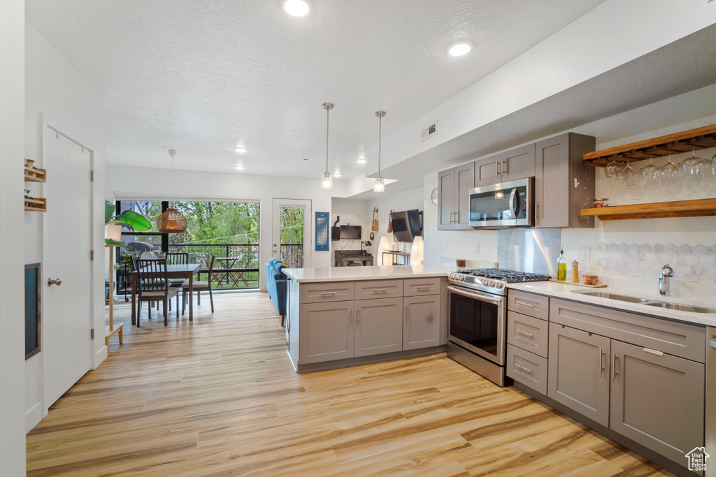 Kitchen featuring light wood-type flooring, kitchen peninsula, stainless steel appliances, sink, and tasteful backsplash