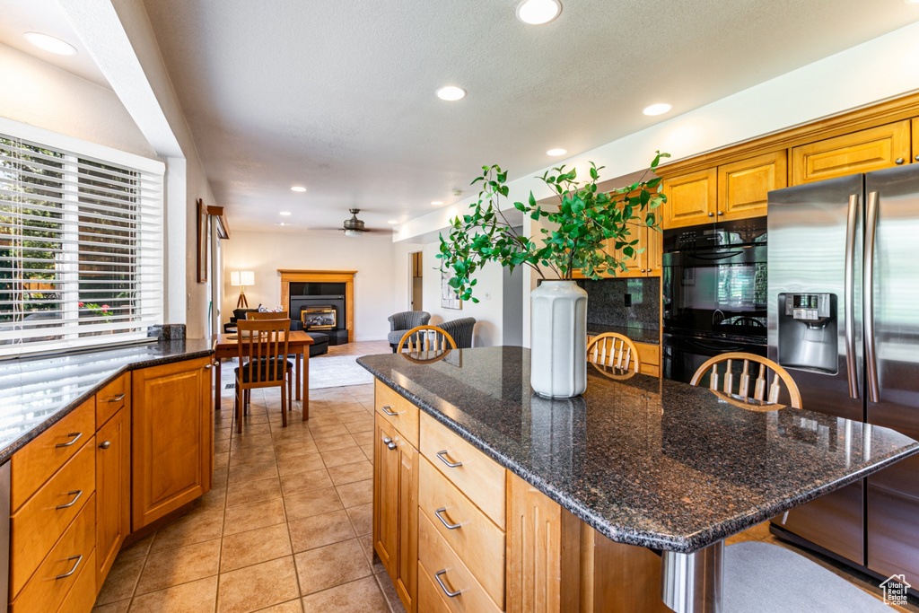 Kitchen with a center island, a kitchen breakfast bar, stainless steel refrigerator with ice dispenser, light tile floors, and dark stone countertops