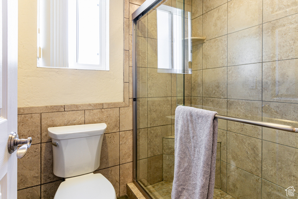 Bathroom featuring an enclosed shower, toilet, and tile walls