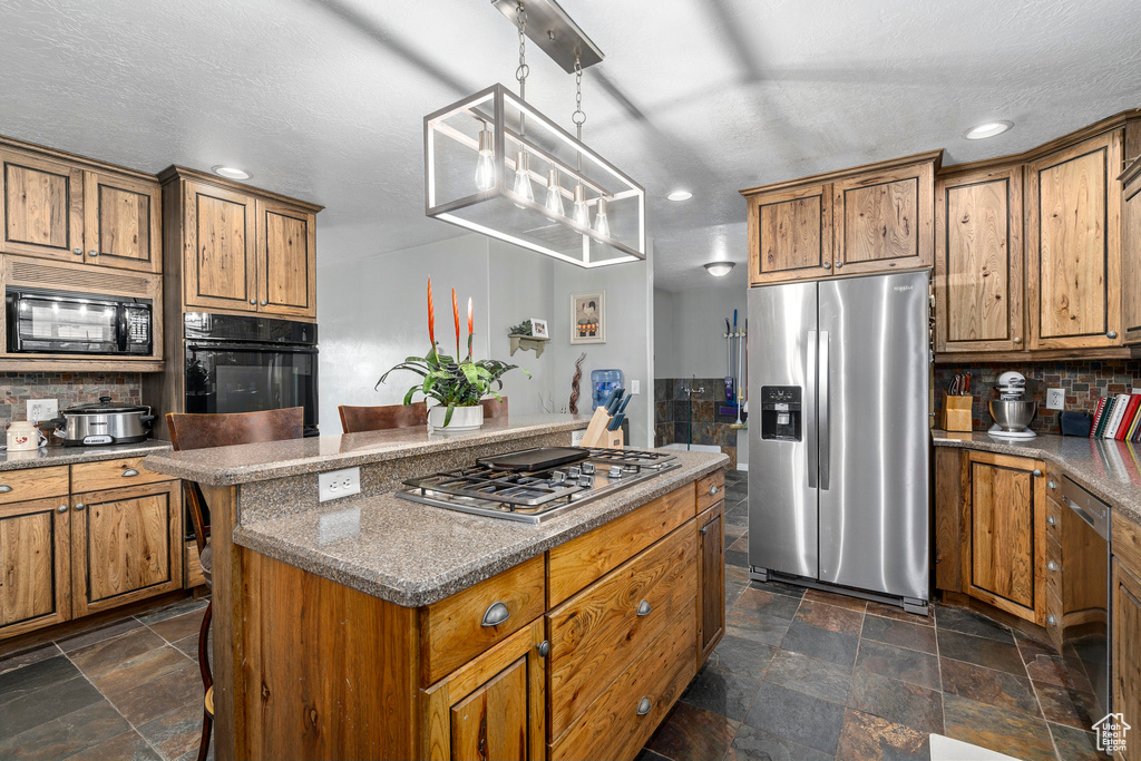 Kitchen featuring tasteful backsplash, dark tile floors, a center island, and black appliances