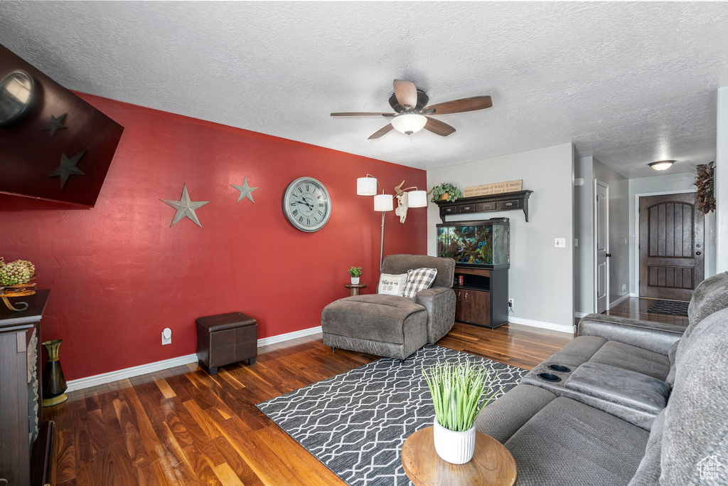 Living room with a textured ceiling, ceiling fan, and dark wood-type flooring