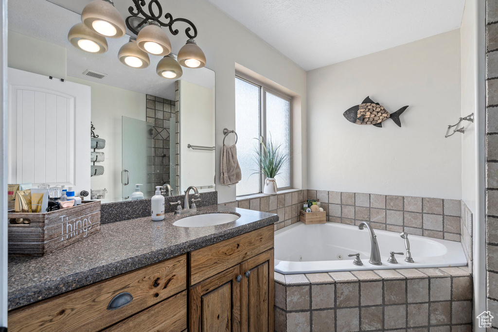 Bathroom featuring vanity with extensive cabinet space, tiled bath, and a notable chandelier