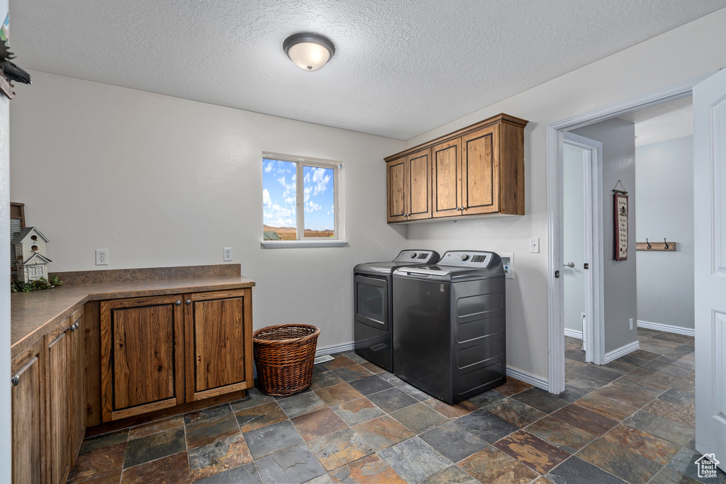 Laundry area featuring dark tile flooring, cabinets, separate washer and dryer, and a textured ceiling