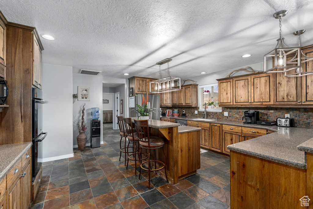 Kitchen featuring a center island, decorative light fixtures, backsplash, dark tile flooring, and stainless steel fridge