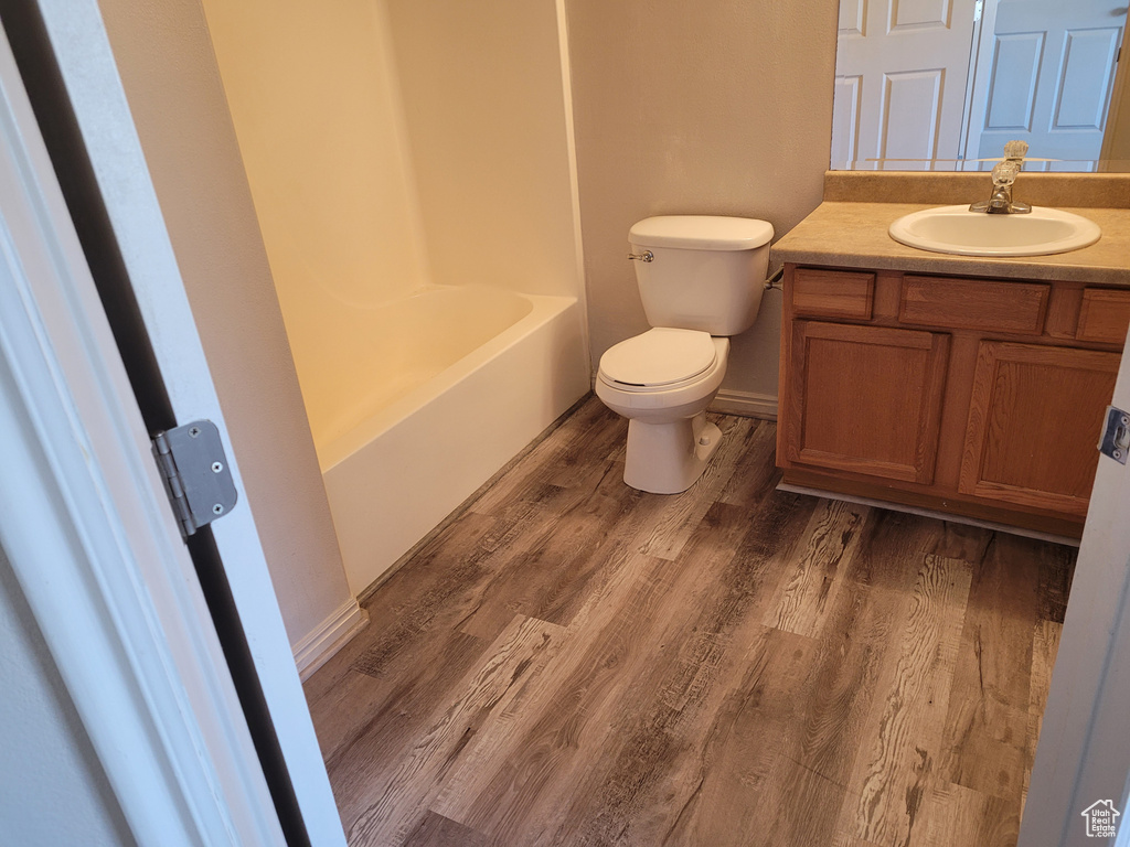 Full bathroom with wood-type flooring, oversized vanity, toilet, and shower / tub combination