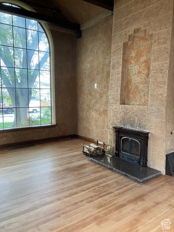 Unfurnished living room with light hardwood / wood-style flooring, a tiled fireplace, and beam ceiling