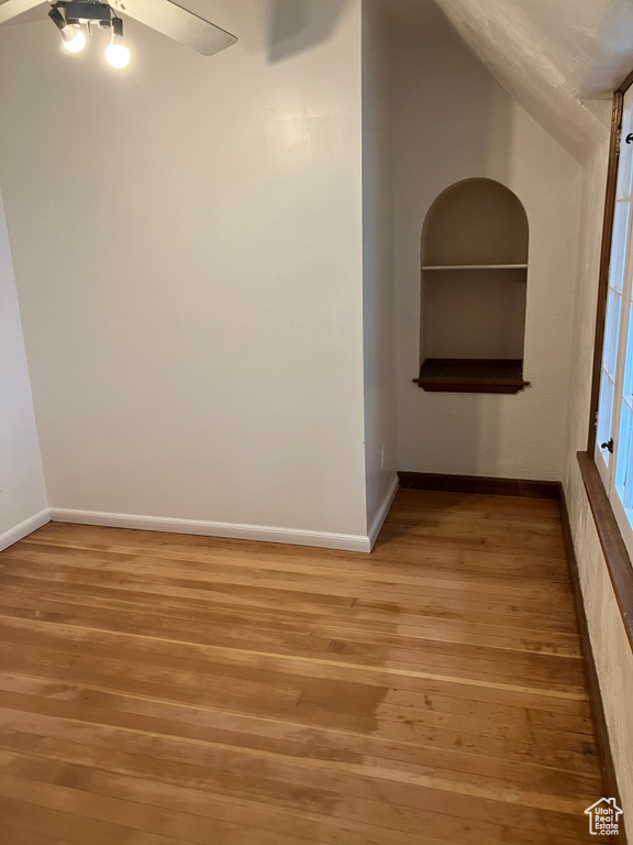 Unfurnished room with vaulted ceiling, ceiling fan, hardwood / wood-style flooring, and built in shelves