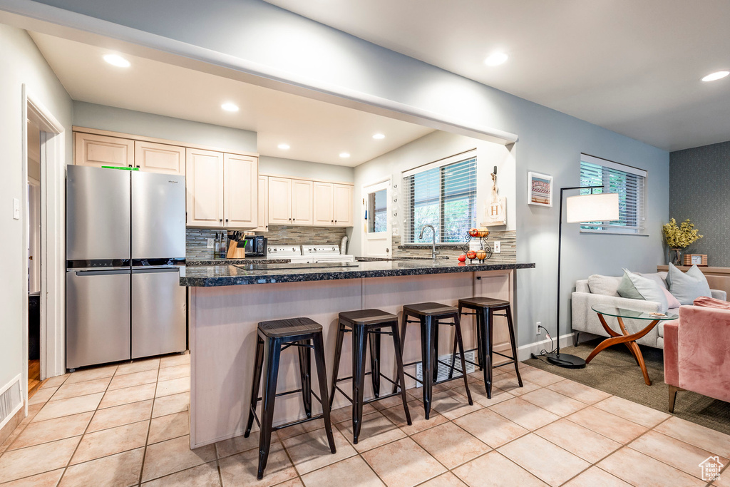 Kitchen featuring a kitchen bar, stainless steel fridge, tasteful backsplash, and light tile floors