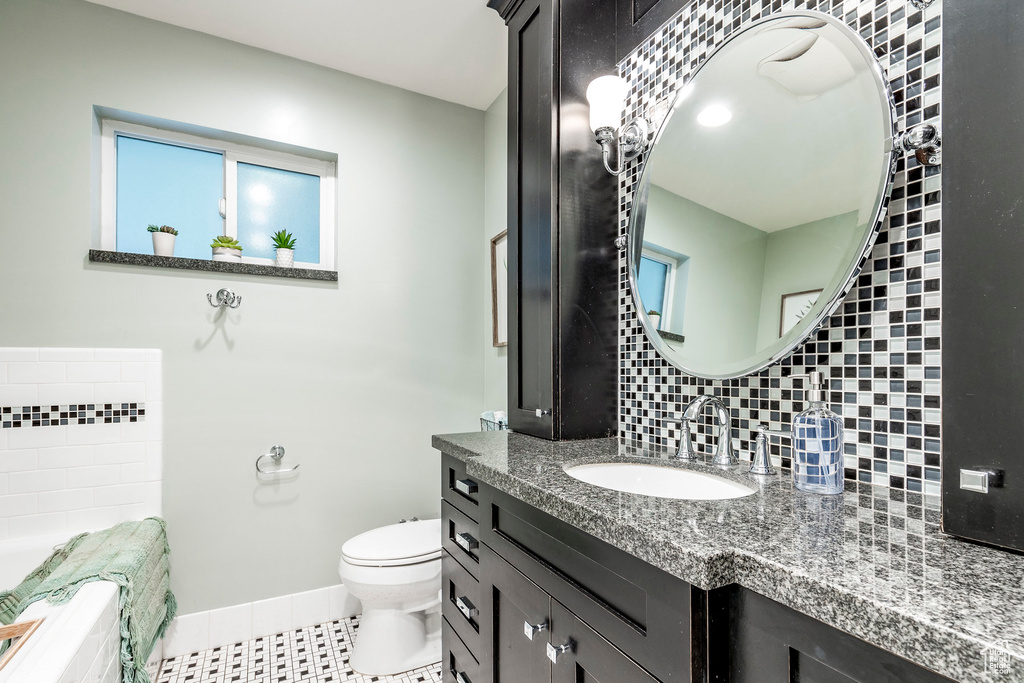 Bathroom with tile floors, vanity with extensive cabinet space, backsplash, and toilet