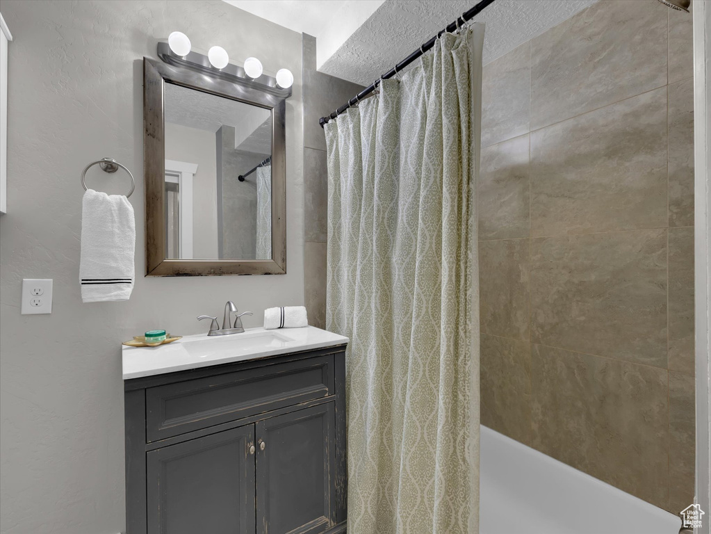 Bathroom with vanity with extensive cabinet space, shower / bath combo with shower curtain, and a textured ceiling