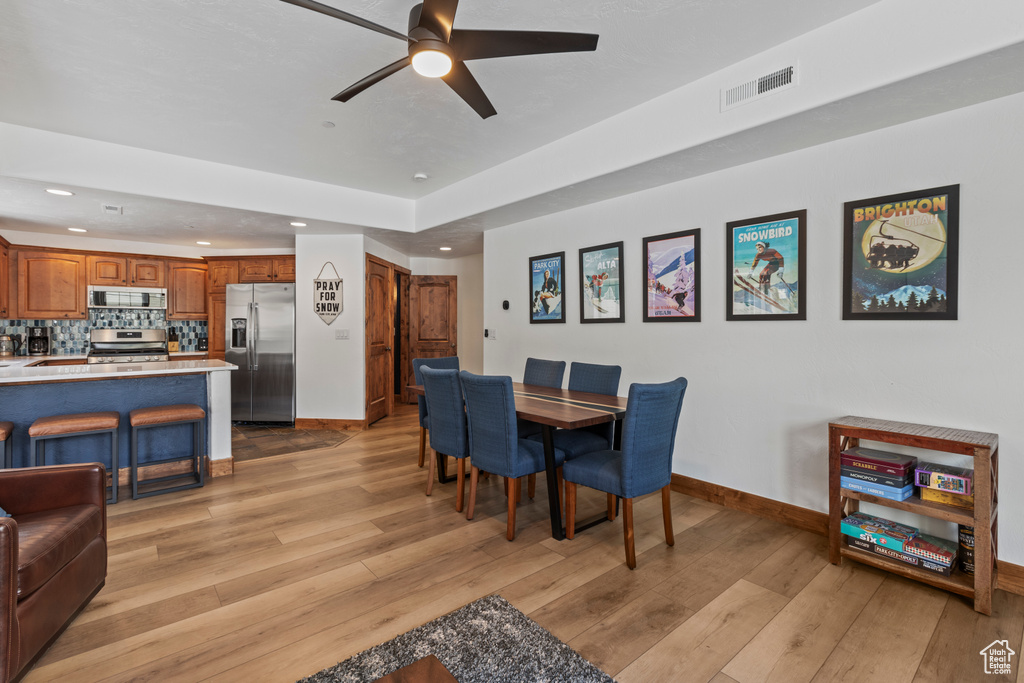 Dining space with light hardwood / wood-style floors, ceiling fan, and a raised ceiling