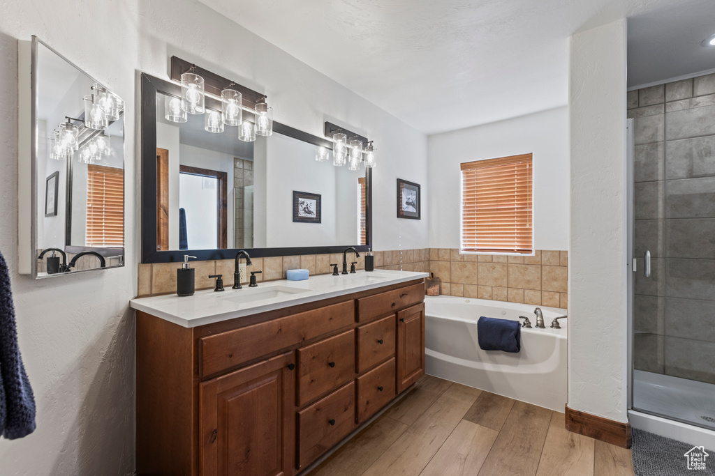Bathroom featuring double vanity, wood-type flooring, a healthy amount of sunlight, and plus walk in shower