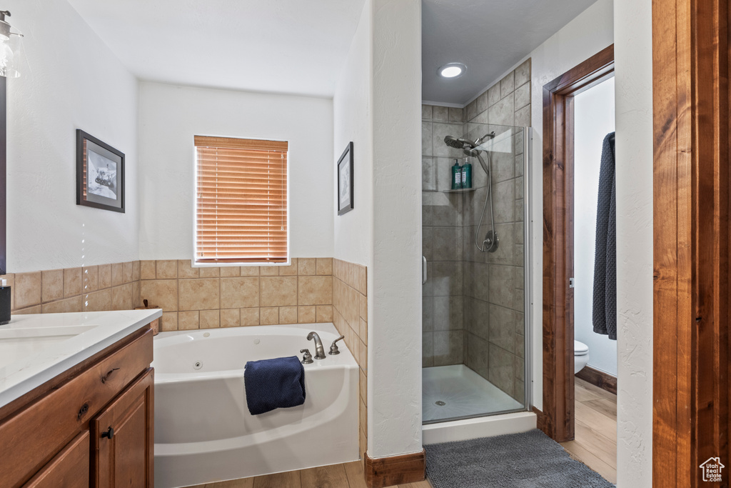 Full bathroom with shower with separate bathtub, vanity, toilet, a healthy amount of sunlight, and hardwood / wood-style flooring