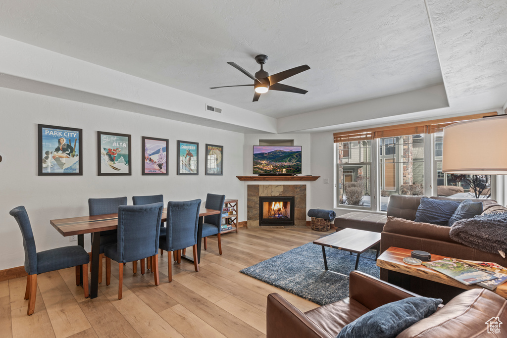 Living room featuring a tray ceiling, light hardwood / wood-style flooring, ceiling fan, and a tile fireplace