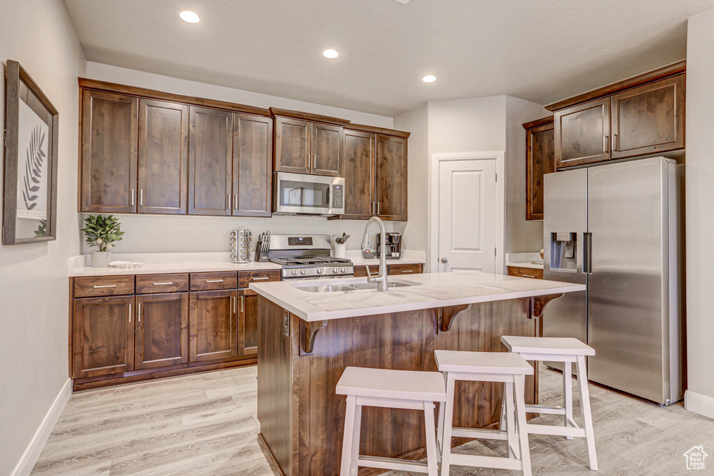 Kitchen featuring appliances with stainless steel finishes, light hardwood / wood-style flooring, sink, dark brown cabinets, and an island with sink