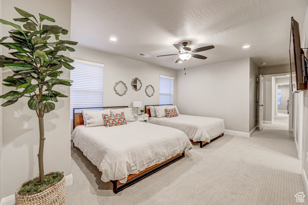 Bedroom featuring light colored carpet, multiple windows, and ceiling fan