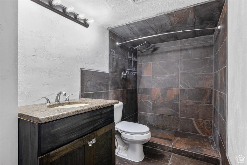 Bathroom with tiled shower, tile walls, vanity, tile flooring, and toilet