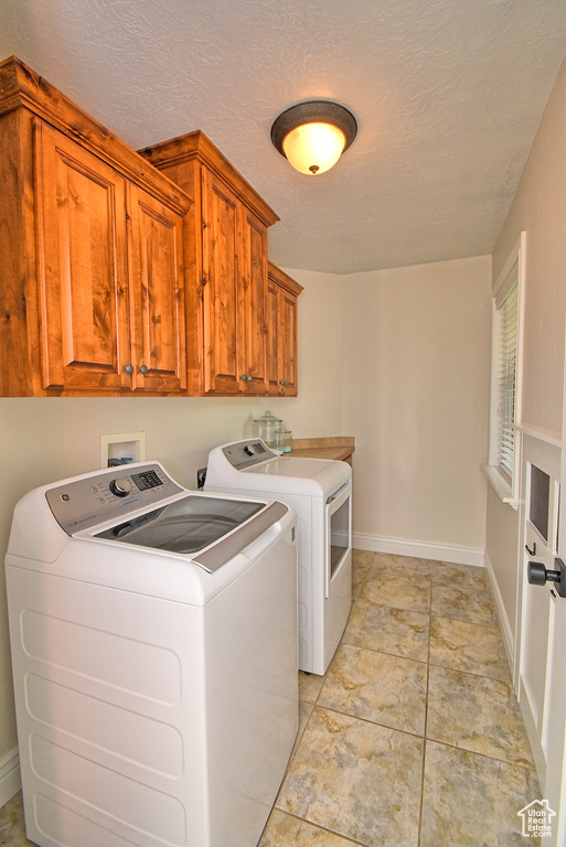 Clothes washing area featuring washer and clothes dryer, cabinets, a textured ceiling, and light tile flooring