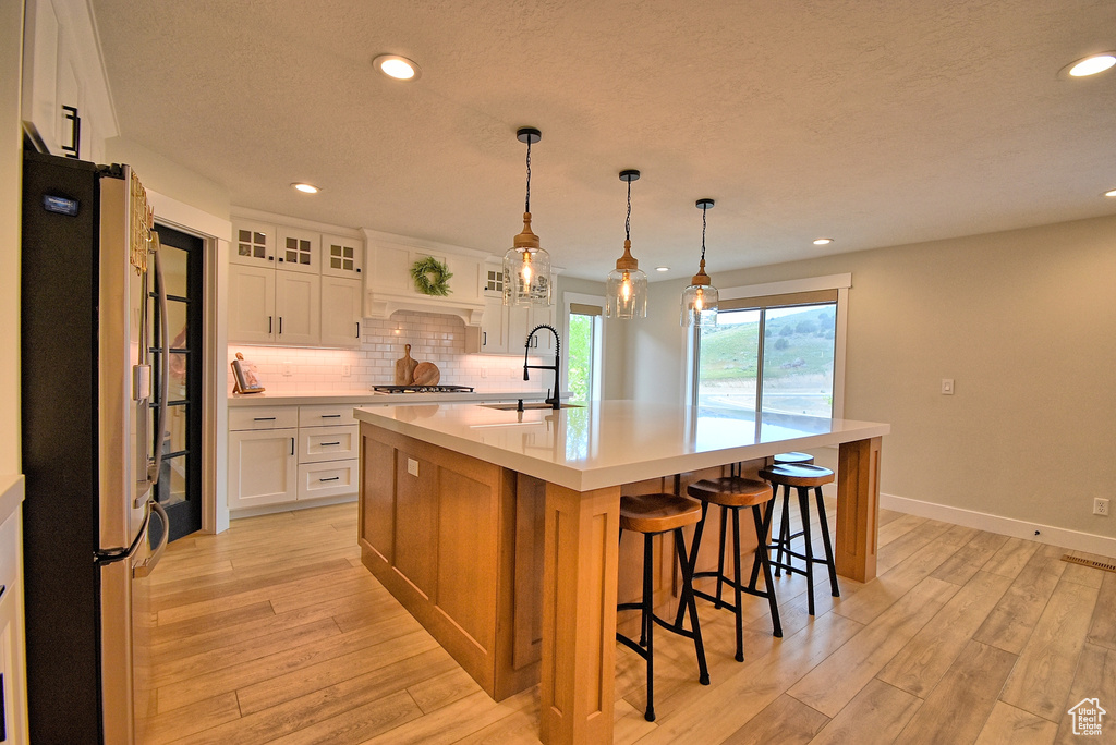 Kitchen with appliances with stainless steel finishes, light hardwood / wood-style flooring, white cabinets, backsplash, and a center island with sink