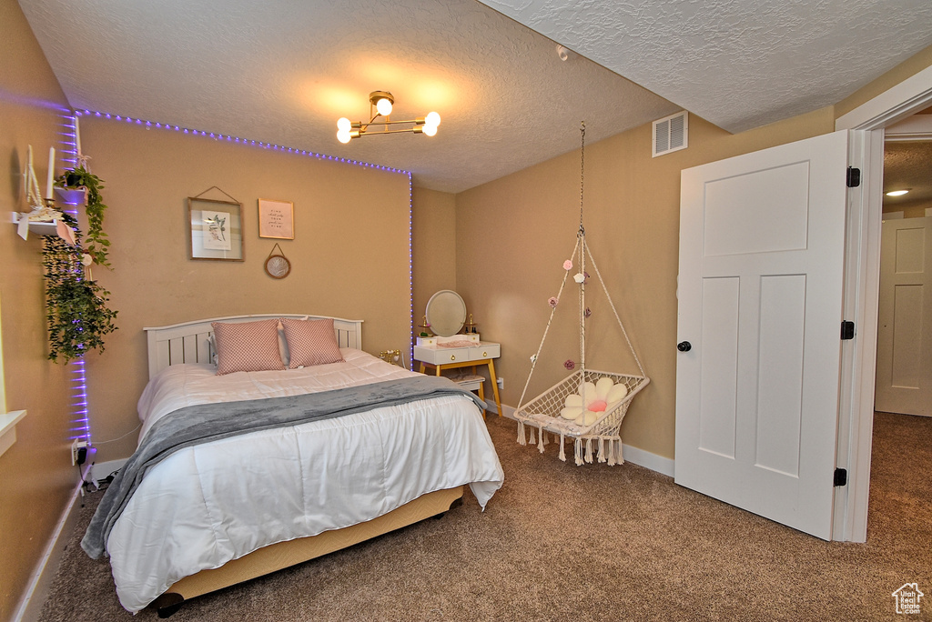 Carpeted bedroom featuring a chandelier and a textured ceiling