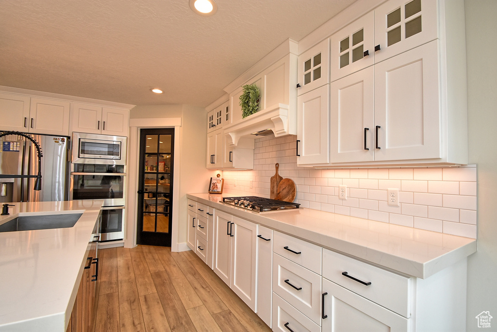 Kitchen featuring white cabinets, stainless steel appliances, light hardwood / wood-style floors, and backsplash