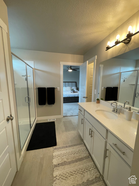 Bathroom featuring an enclosed shower, wood-type flooring, large vanity, ceiling fan, and a textured ceiling