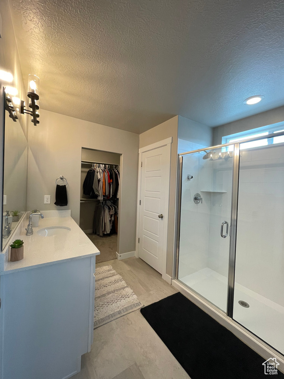 Bathroom with a shower with shower door, vanity, and a textured ceiling