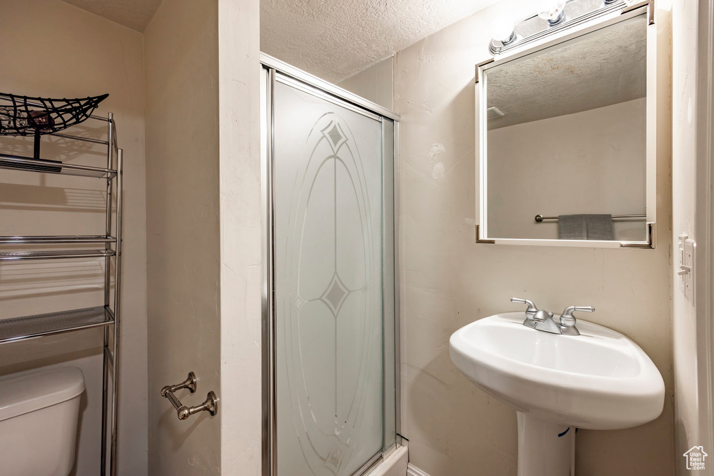 Bathroom with a textured ceiling, a shower with shower door, and toilet