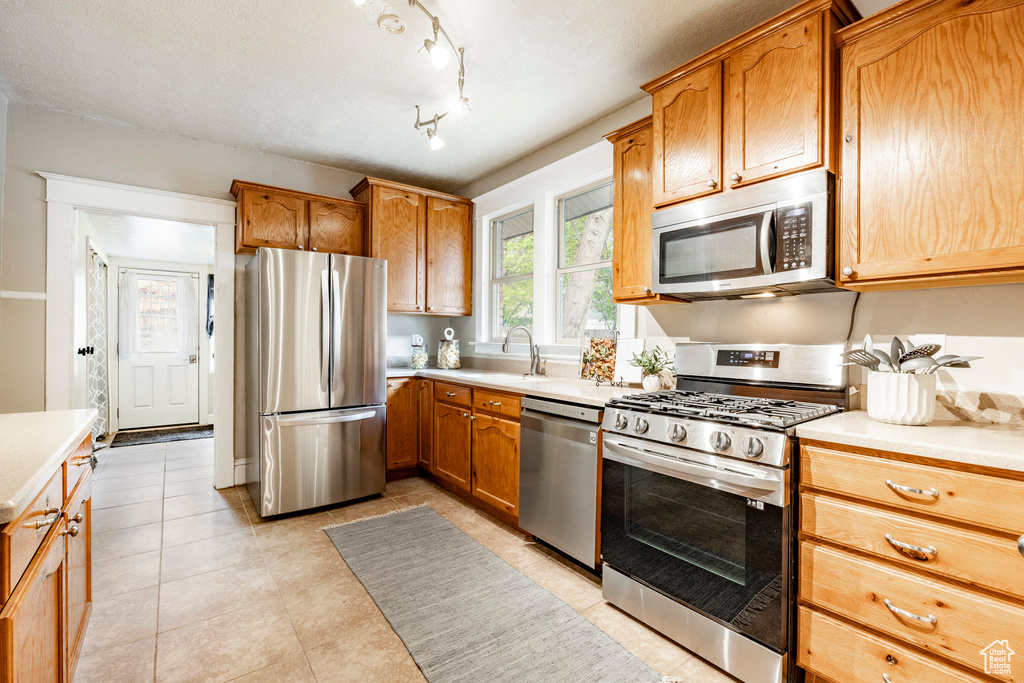 Kitchen featuring sink, track lighting, stainless steel appliances, and light tile floors