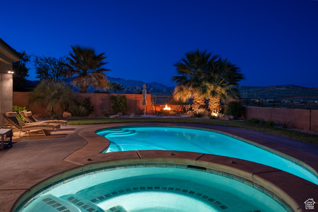 Pool at twilight featuring a mountain view, an in ground hot tub, and a patio
