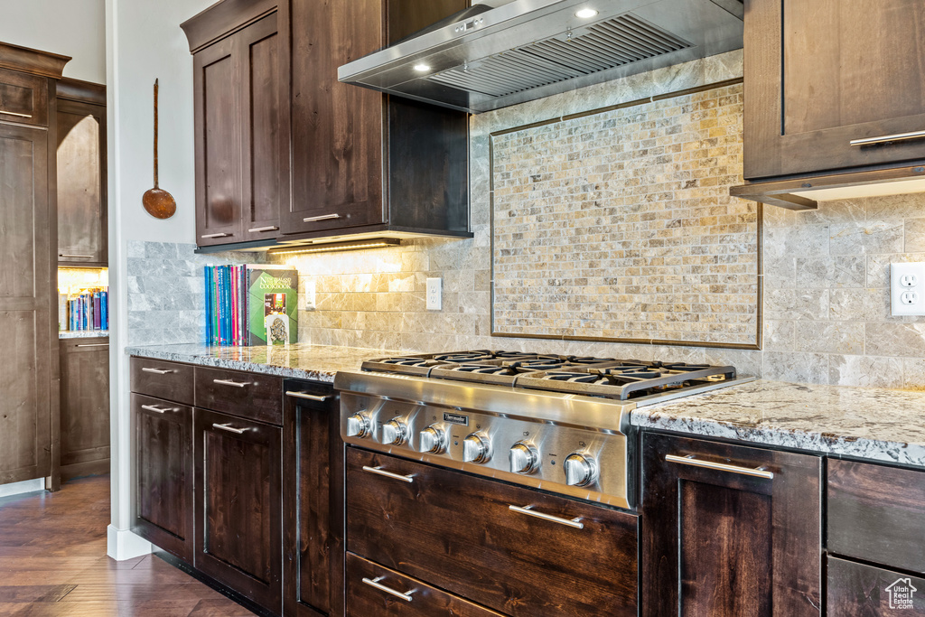 Kitchen with backsplash, dark brown cabinetry, dark wood-type flooring, and wall chimney range hood
