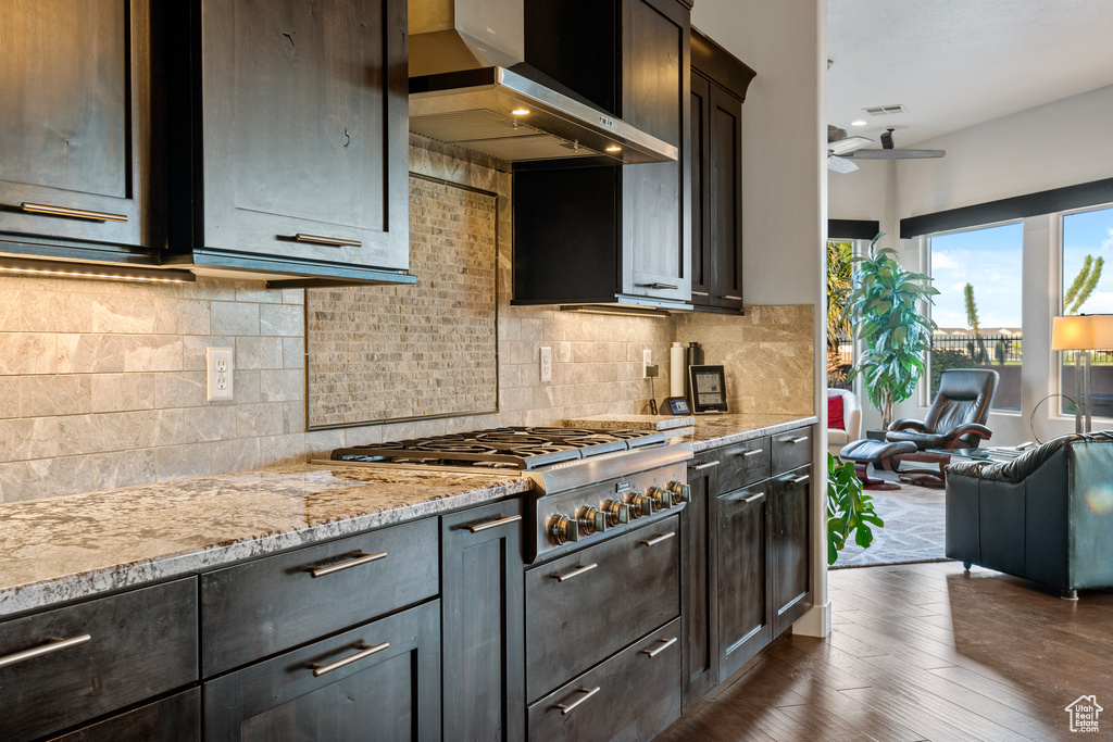 Kitchen featuring wall chimney exhaust hood, dark hardwood / wood-style floors, backsplash, dark brown cabinets, and ceiling fan