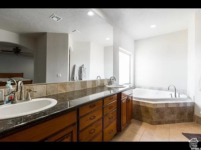 Bathroom featuring double vanity, a relaxing tiled bath, and tile floors
