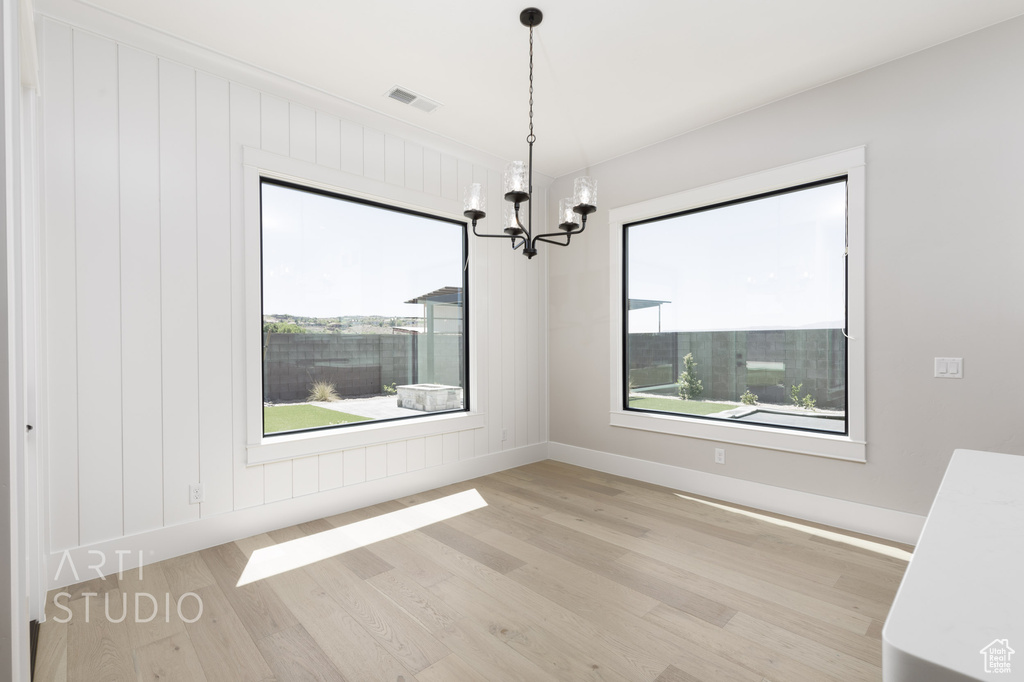 Unfurnished room featuring light hardwood / wood-style flooring, an inviting chandelier, and plenty of natural light
