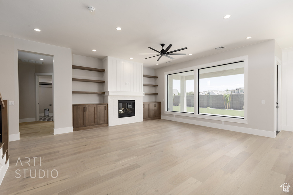 Unfurnished living room with a large fireplace, light hardwood / wood-style flooring, and ceiling fan