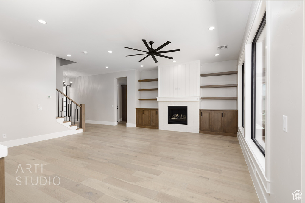 Unfurnished living room featuring light hardwood / wood-style flooring, ceiling fan, and a large fireplace