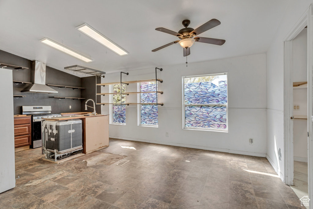 Kitchen with stove, wall chimney range hood, tile floors, and ceiling fan