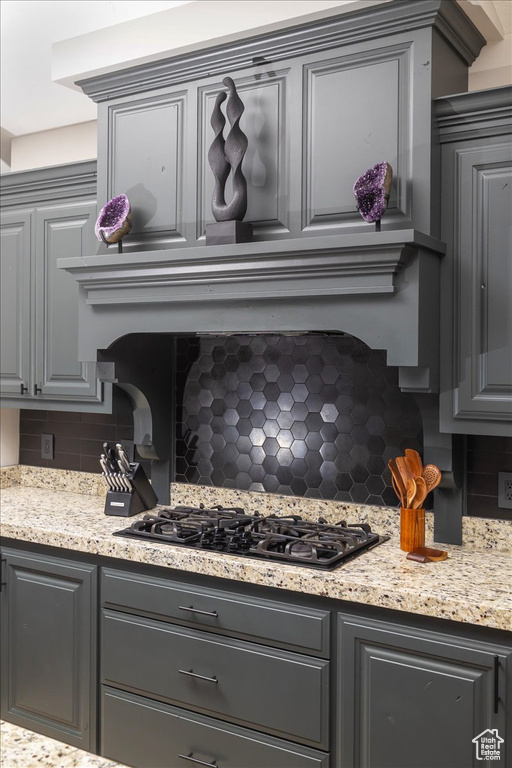 Kitchen featuring tasteful backsplash, black gas cooktop, gray cabinetry, and light stone counters